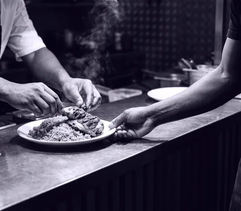 Hands passing a plated meal across a restaurant kitchen pass